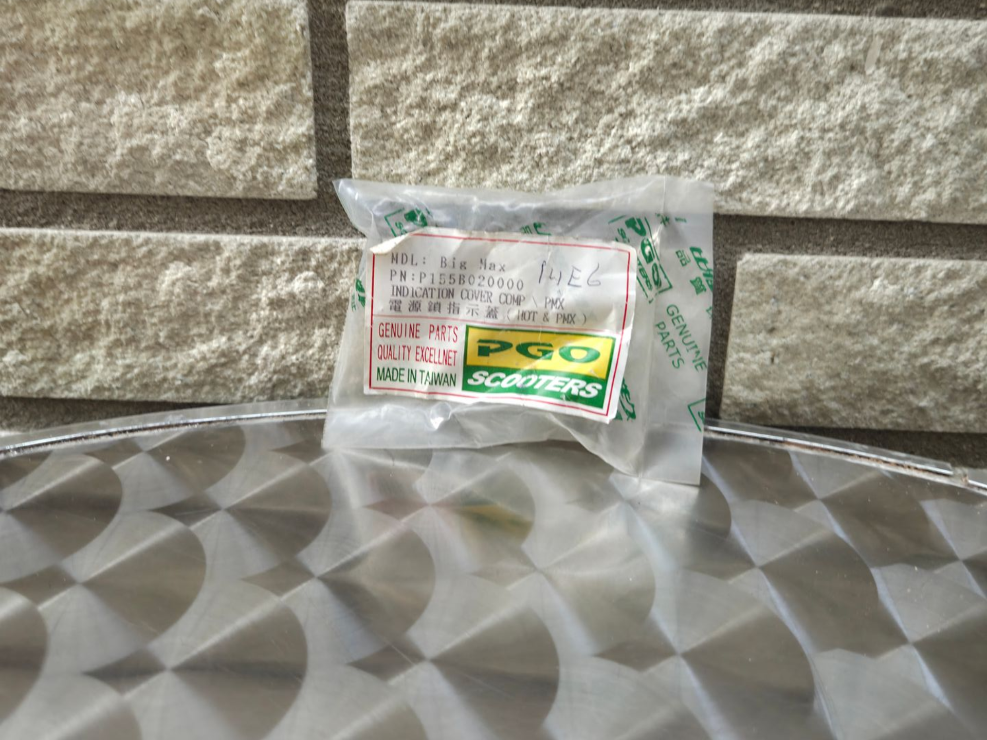 Een klein, doorzichtig plastic zakje met een etiket, dat op een grijs, bedrukt oppervlak tegen een stenen muur ligt.