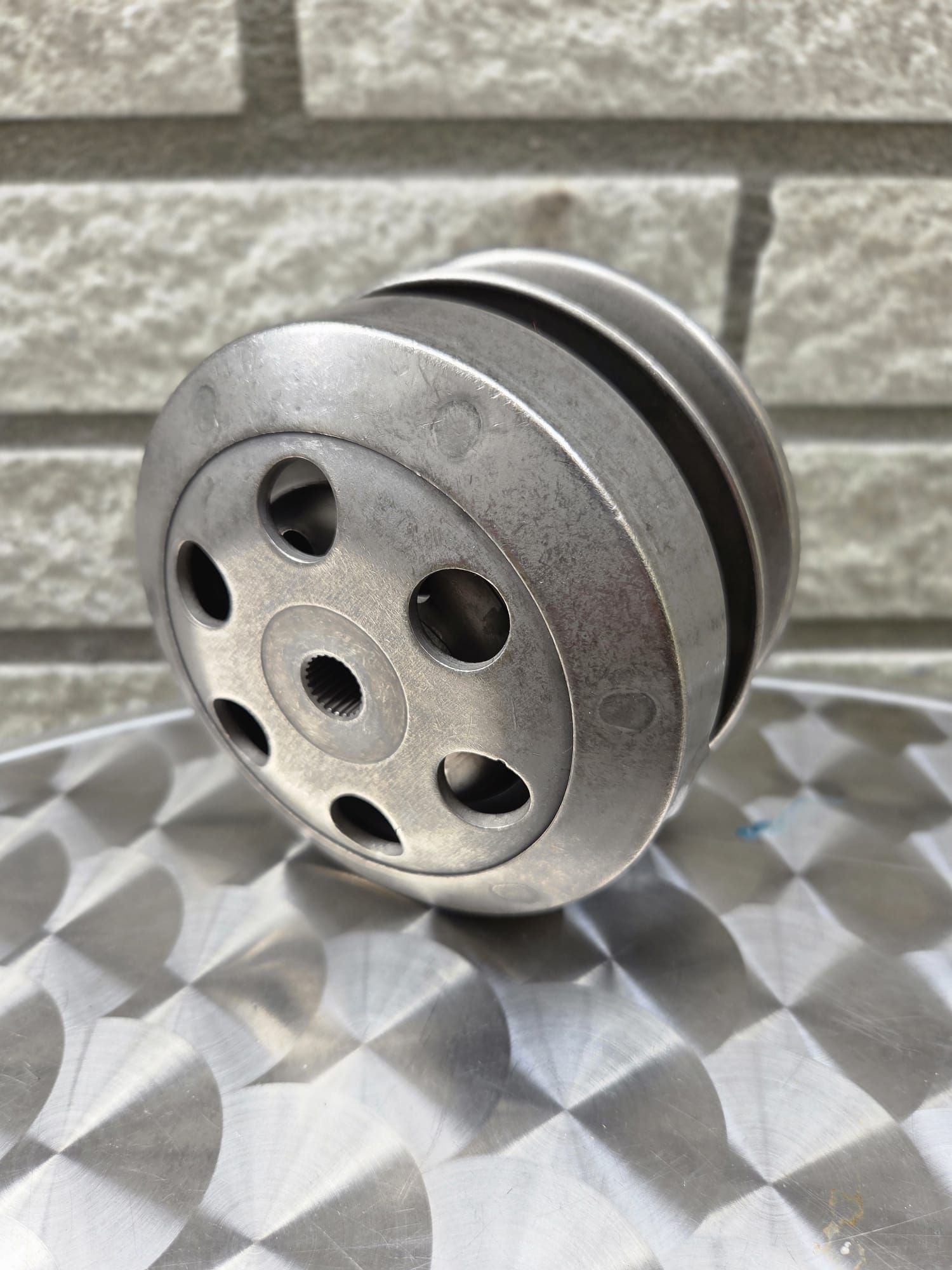 Metalen katrol met meerdere cirkelvormige niveaus en een gatenpatroon, op een gestructureerd oppervlak.
