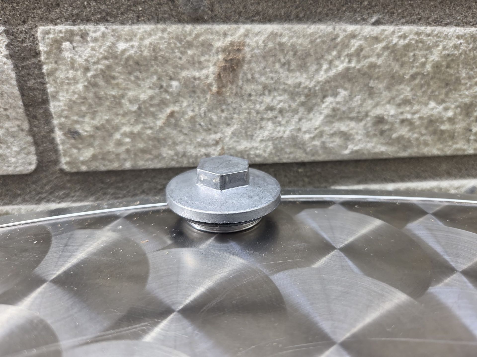 Zilverkleurige boutkop en sluitring op een geborsteld metalen oppervlak, tegen een lichtgekleurde bakstenen muur.