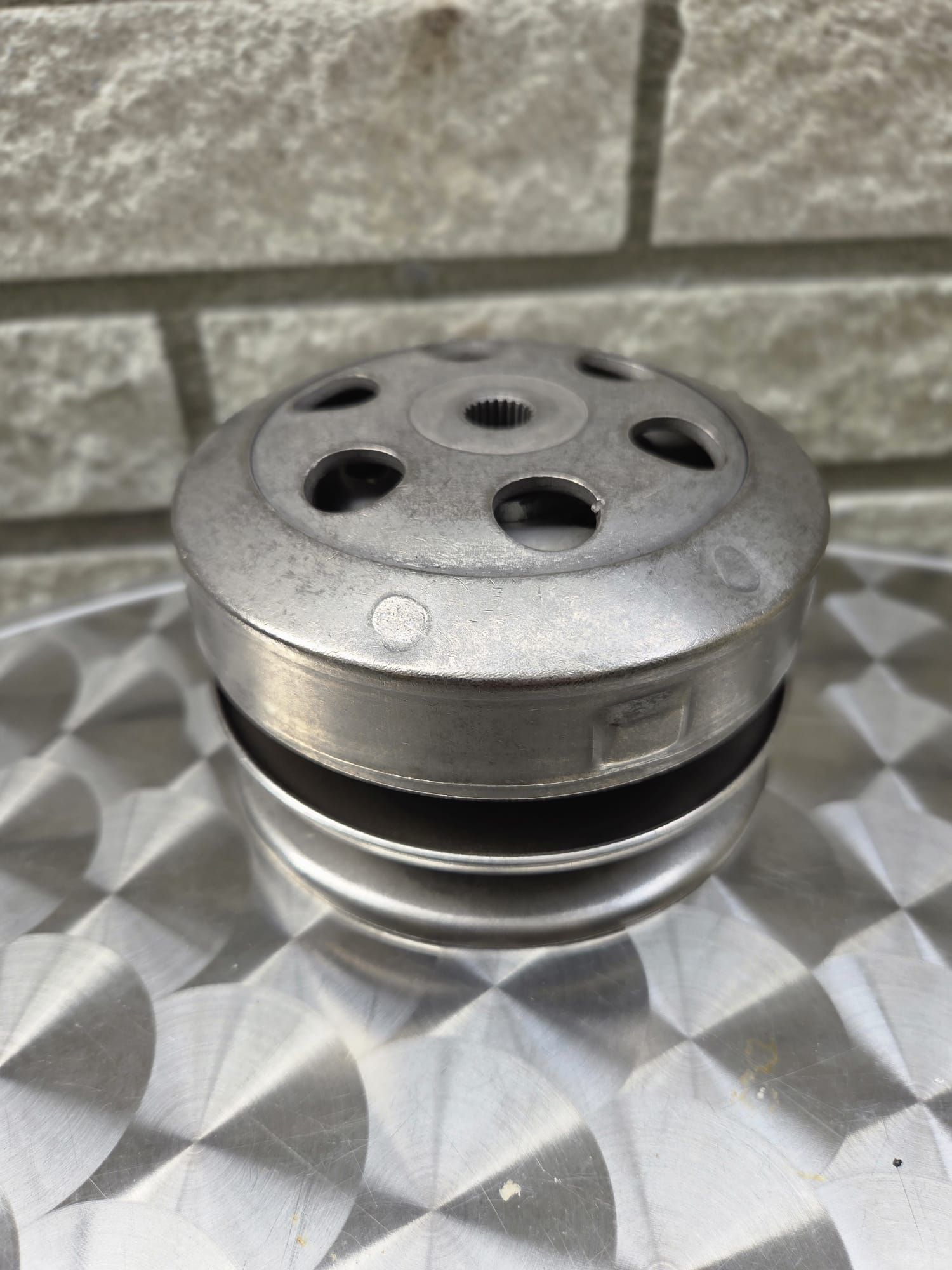 Metalen katrol met meerdere cirkelvormige niveaus en een gatenpatroon, op een gestructureerd oppervlak.