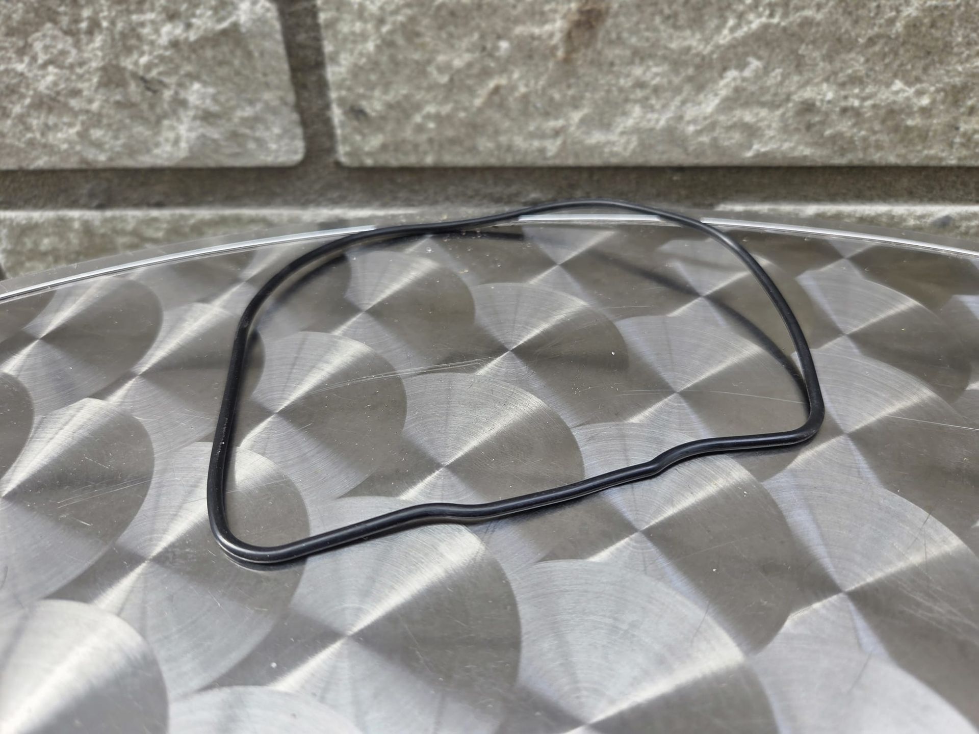 Zwarte rubberen pakking op een zilverkleurig, gestructureerd oppervlak, voor een grijze bakstenen muur.