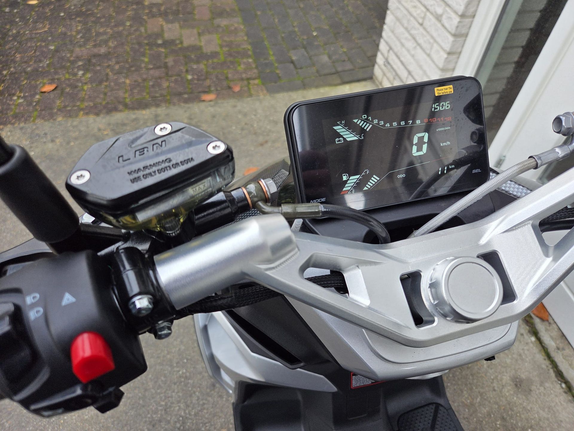 Een zwarte en grijze driewielige scooter met groene accenten staat geparkeerd voor een gebouw met glazen deuren.