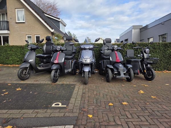 Drie blauw-zwarte elektrische scooters staan geparkeerd bij een donker gebouw.