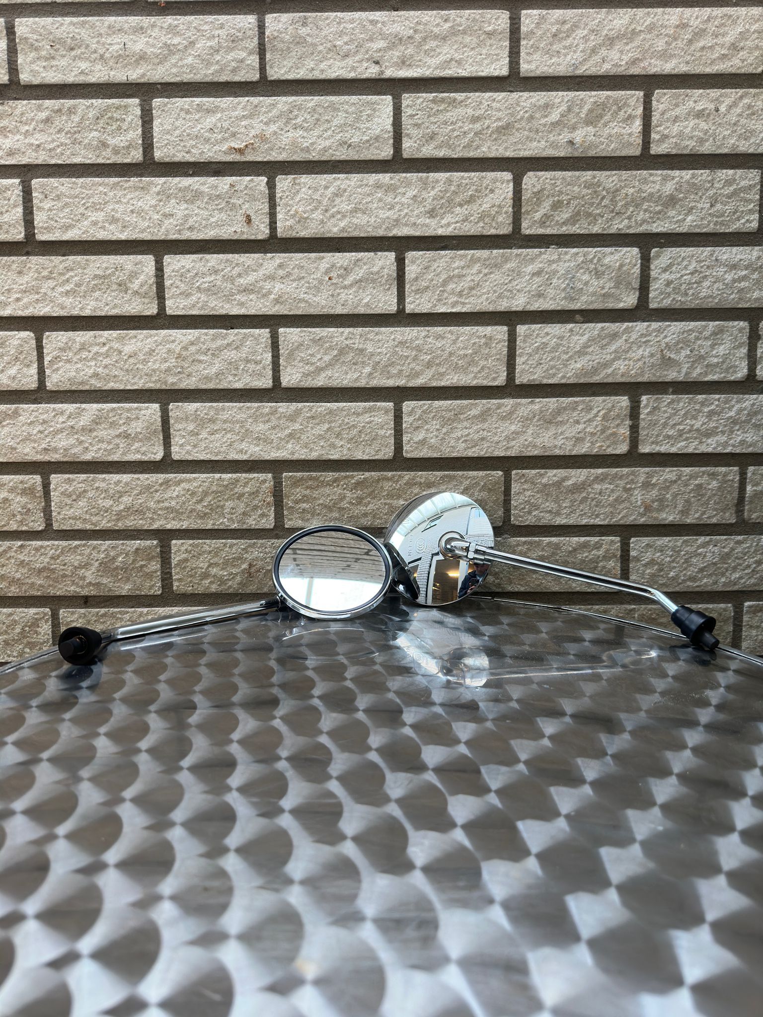 Zonnebril met zwart montuur op een metalen tafel met structuur, tegen een lichtbruine bakstenen muur.