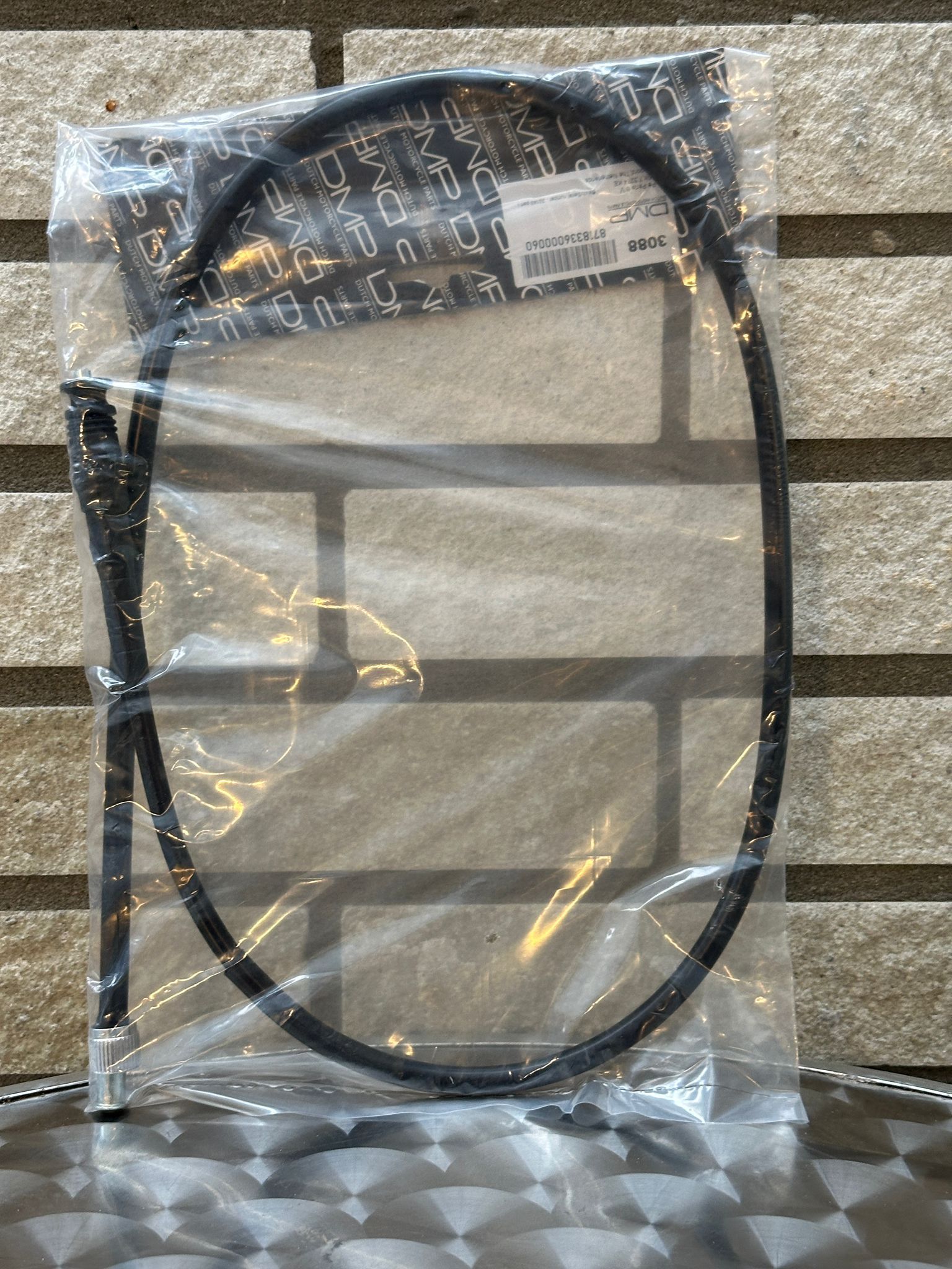 Zwarte kabel met connectoren, verpakt in een transparante plastic zak op een gestreepte ondergrond.