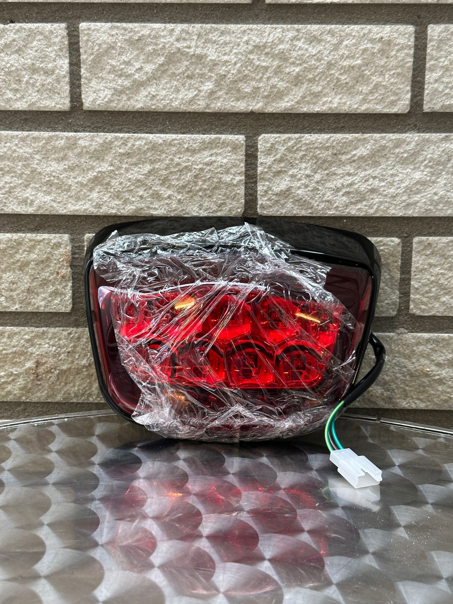 Rood autoachterlicht, in plastic gewikkeld, staat tegen een bakstenen muur op een metalen tafel.