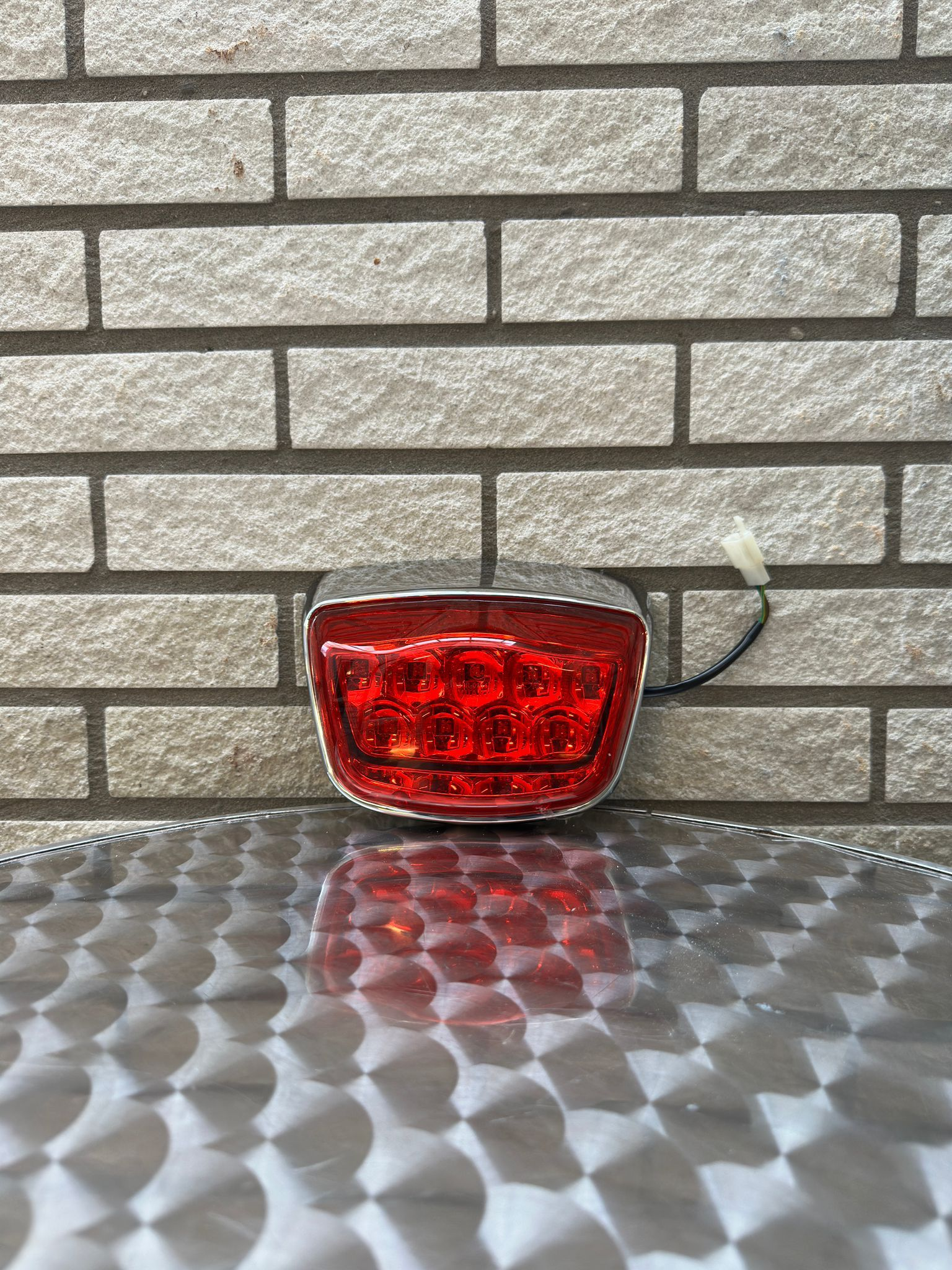 Rood fietsachterlicht op een reflecterend metalen oppervlak tegen een bakstenen muur.