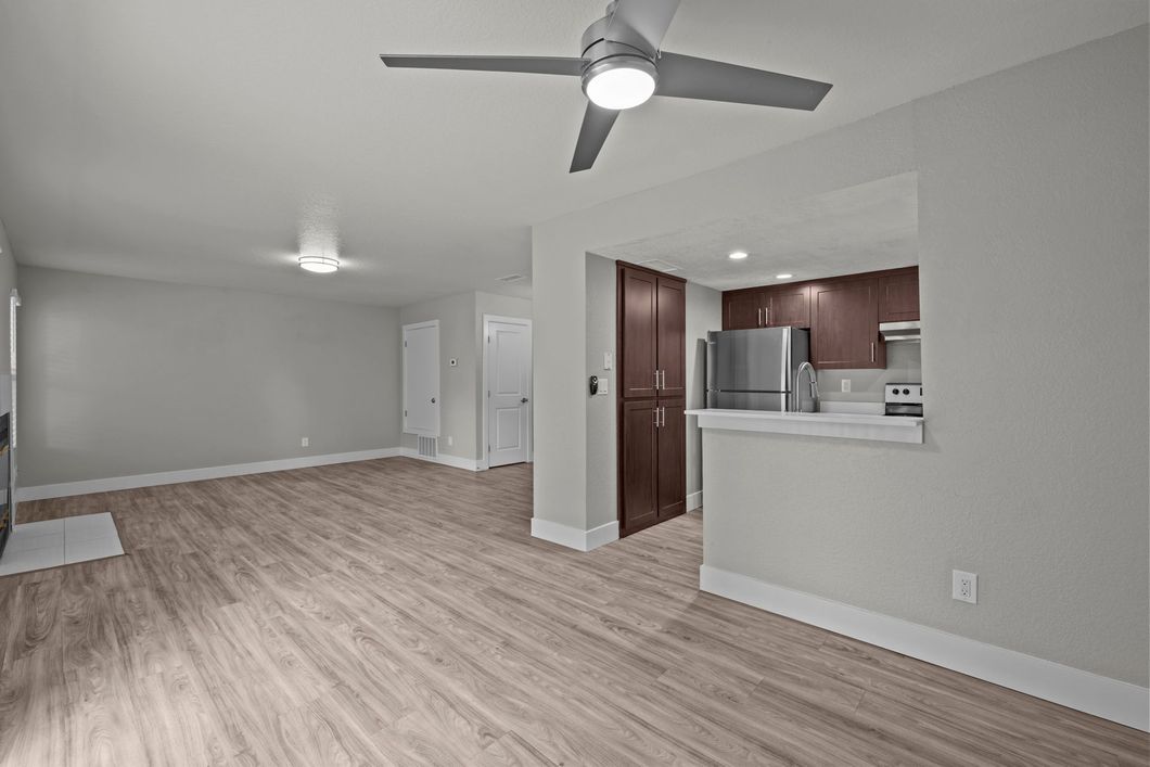 Open-concept modern kitchen and living room with wood floors, gray cabinets, and large windows.