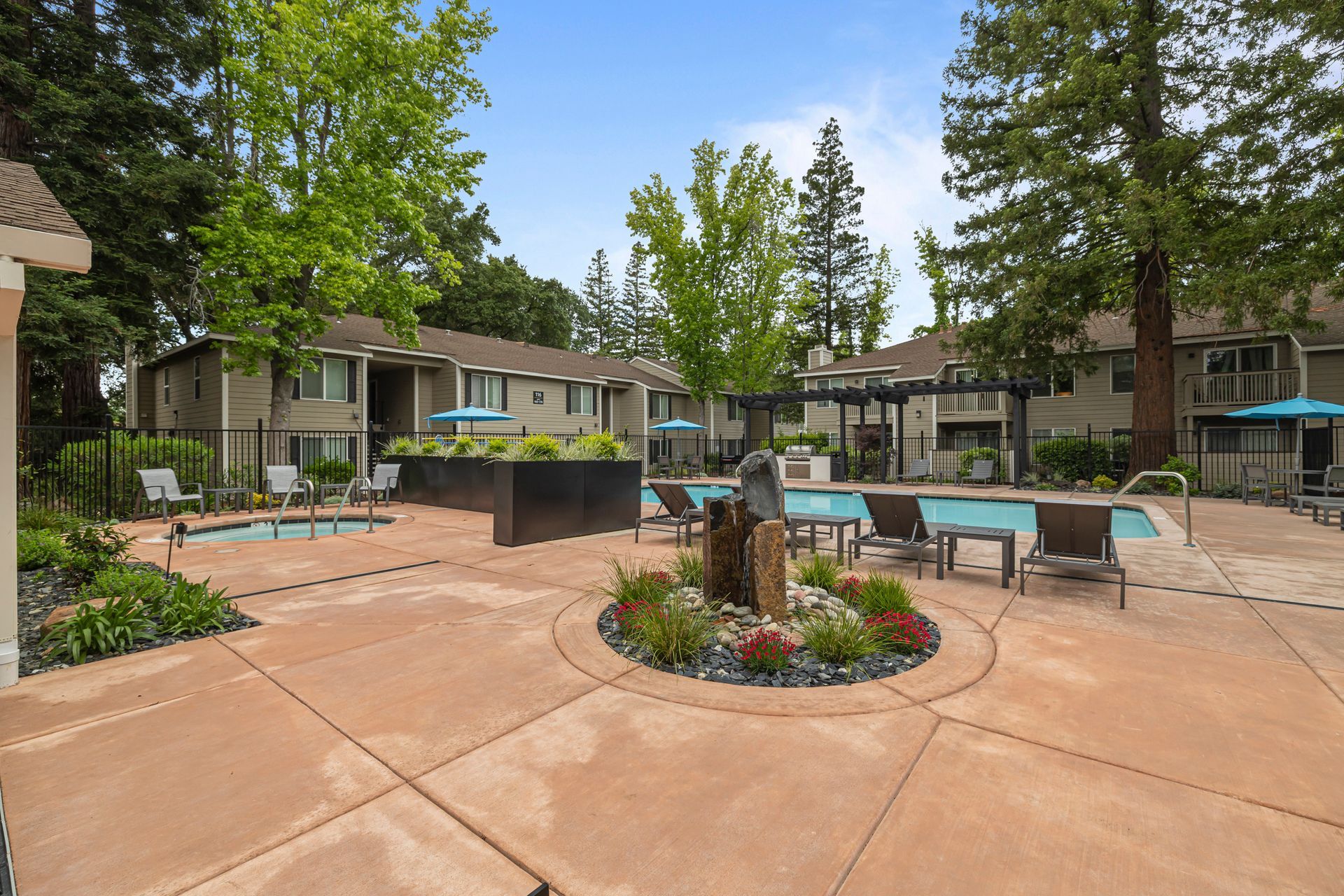 Aerial view of a pool deck with a large rectangular pool, hot tub, lounge chairs, and blue umbrellas.