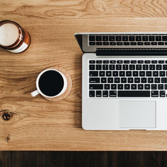 Top-down view of a laptop, coffee mug, and candle on a wooden desk