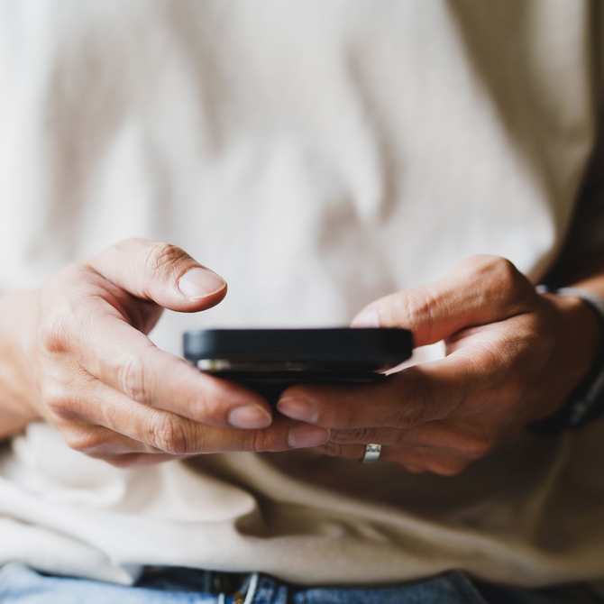Hands holding a black smartphone, typing on screen in a beige shirt