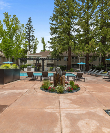 Courtyard pool area with turquoise lounge chairs, trees, and flower beds around a central planter