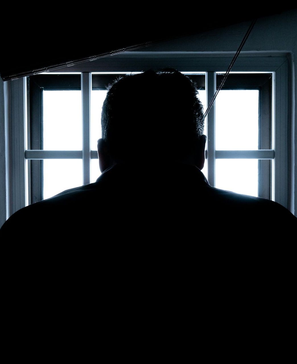Silhouetted person seen from behind in front of a bright barred window