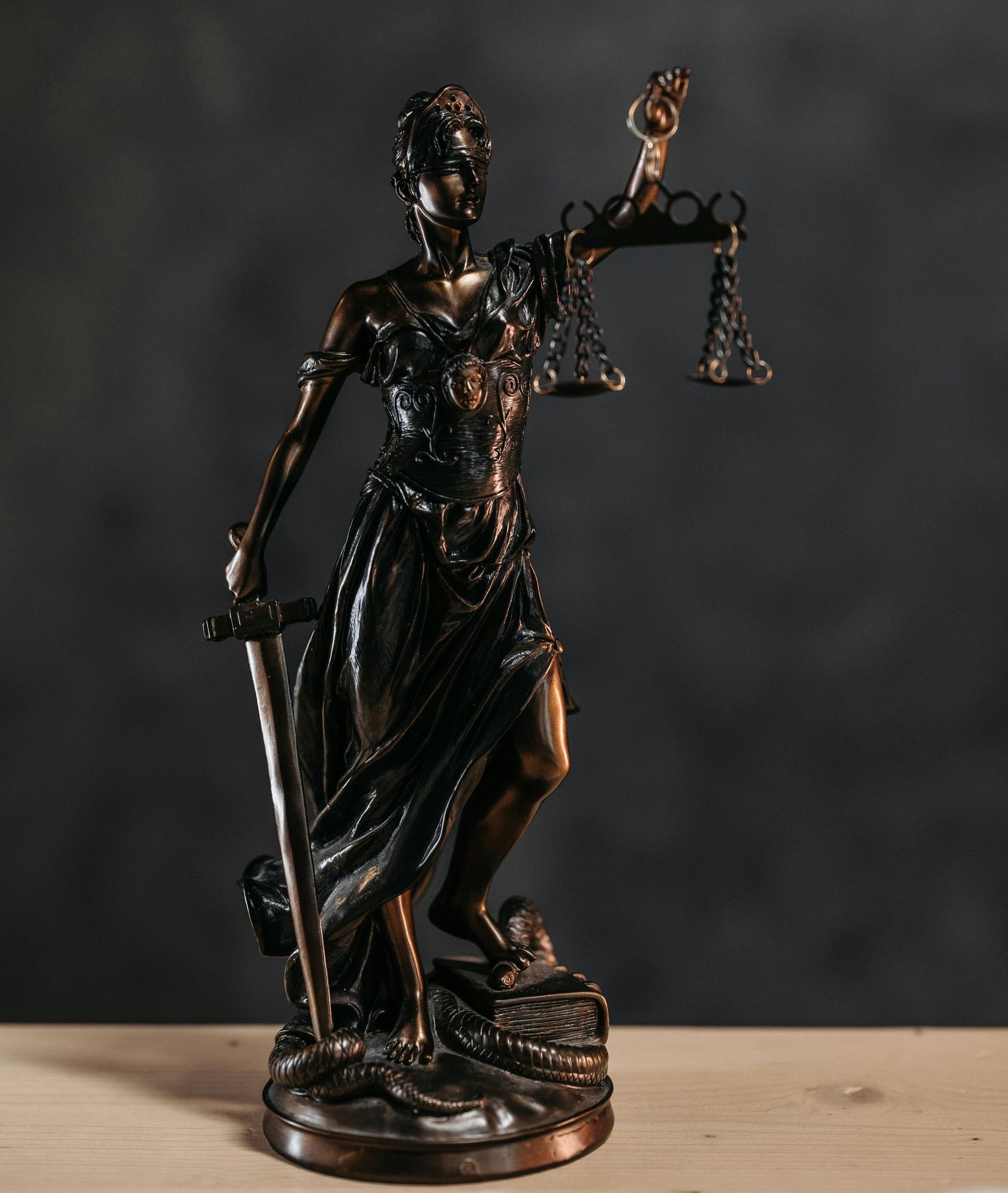 Bronze Lady Justice statue holding scales and sword on a wooden surface