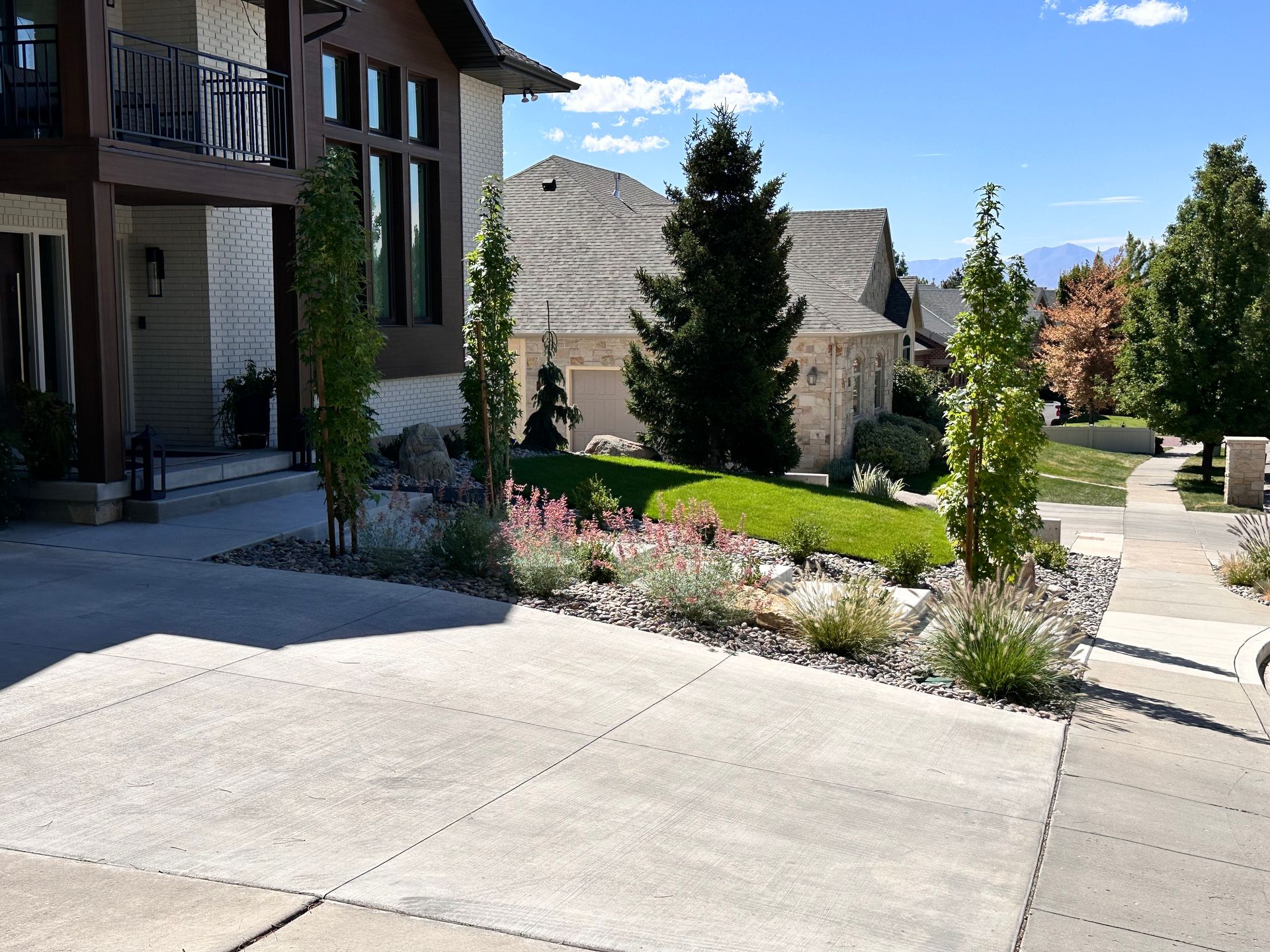 A two-story house with a concrete driveway and landscaped yard on a sunny day.