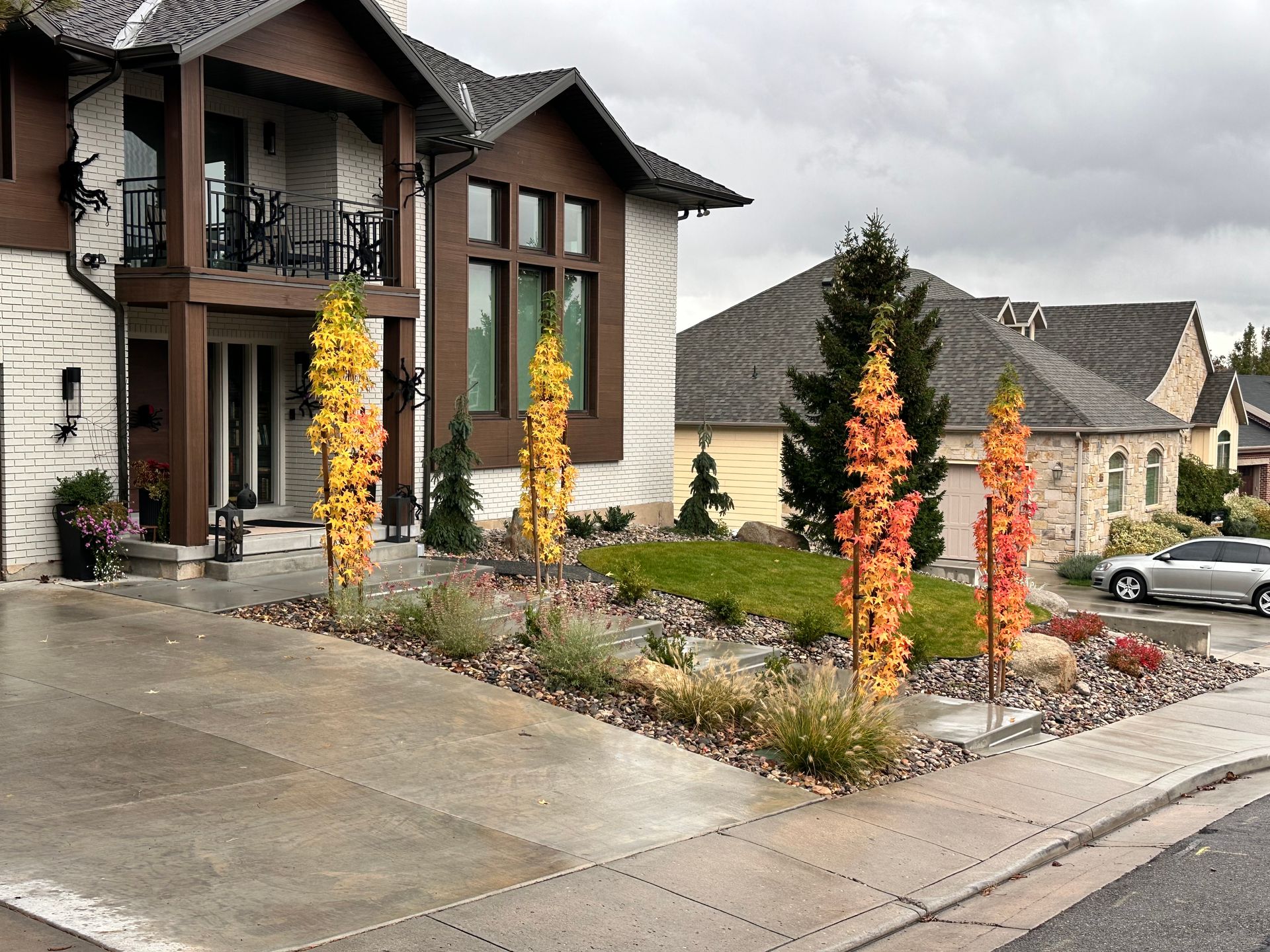 Upscale home with autumn trees, rock garden, and driveway on a wet, cloudy day.