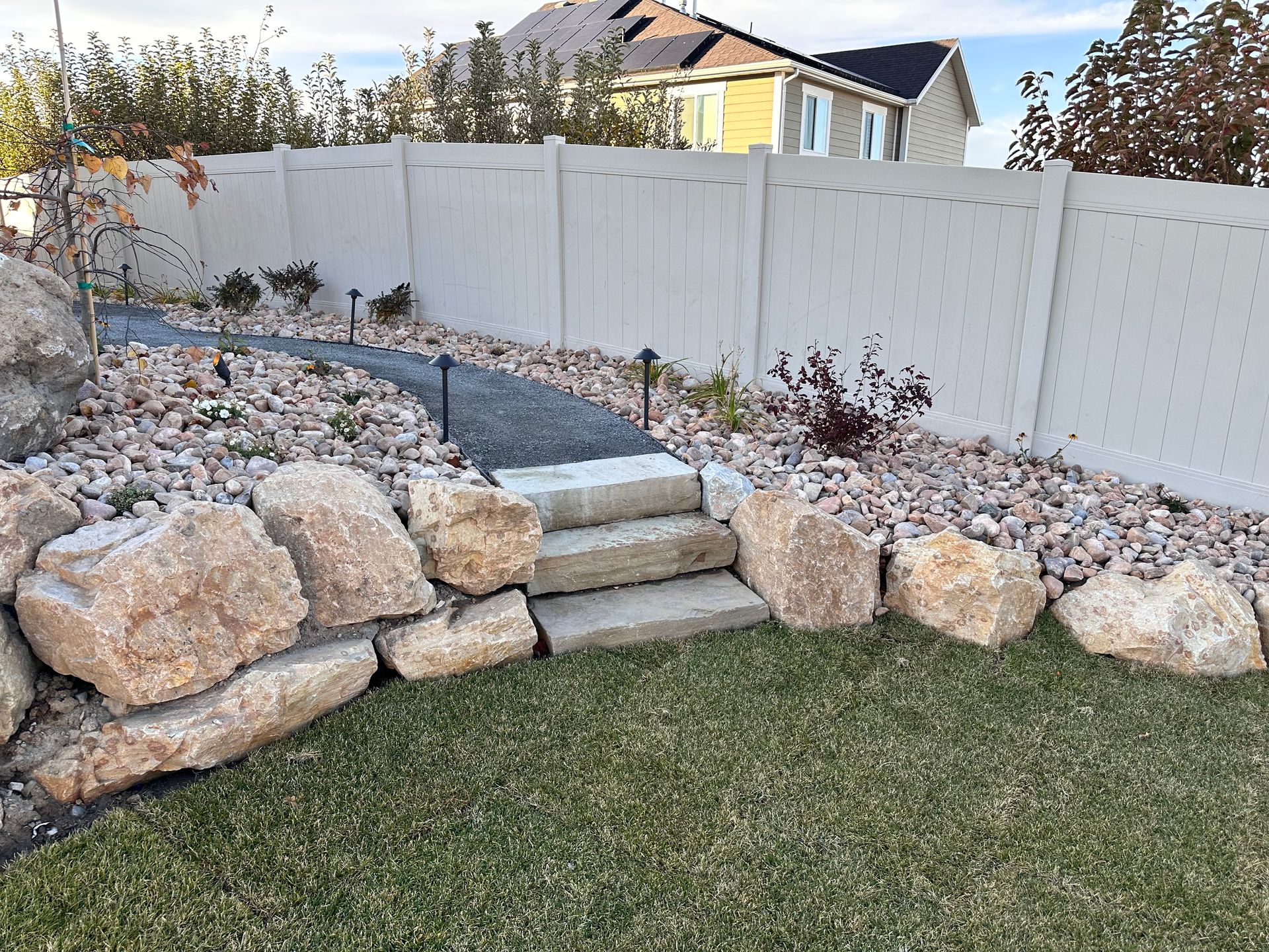 A rock garden with a stone path leading to a white fence, and small steps.