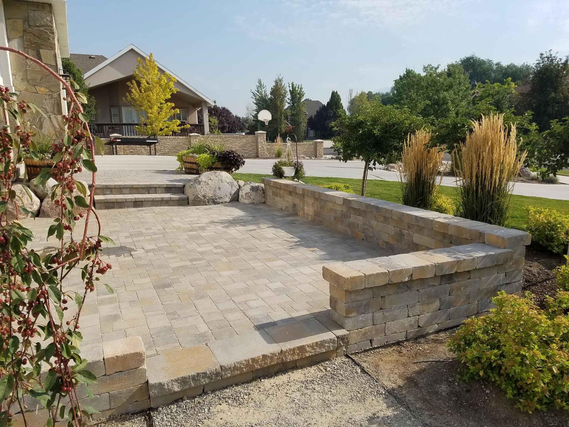 Stone patio with low retaining walls; a house, trees, and greenery are in the background.
