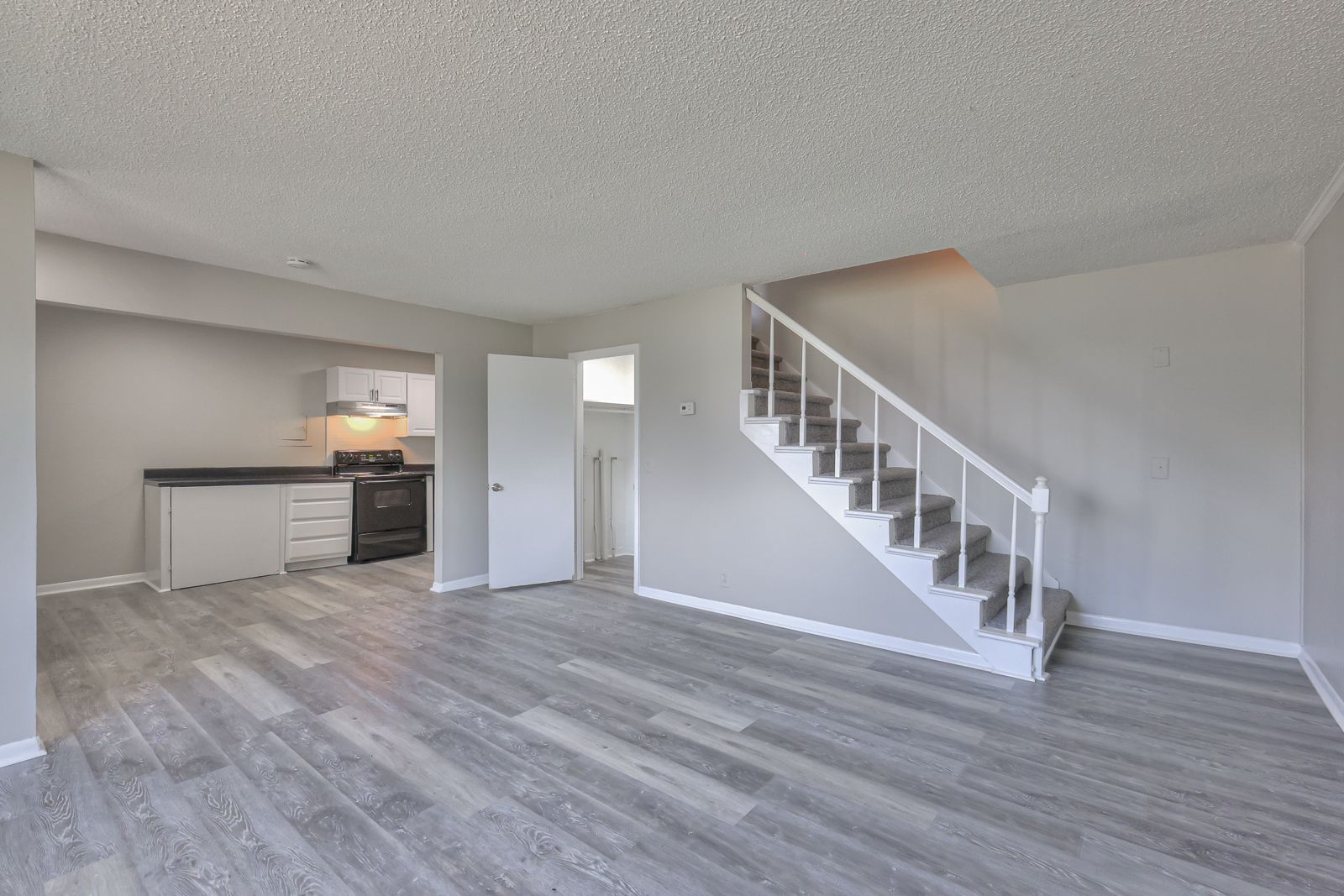 Photo of a large living room, with the kitchen in the left background and the stairs in the right background