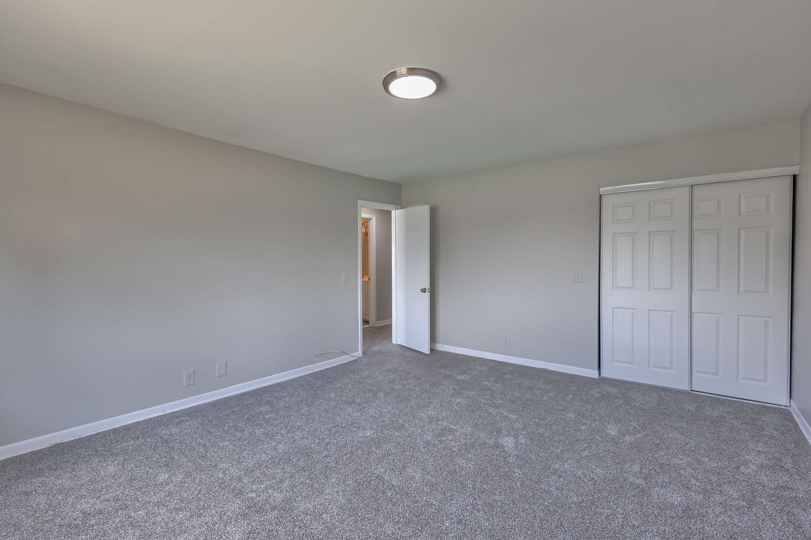 Photo of a large, carpeted bedroom showing a dual door closet and an open door to the hallway