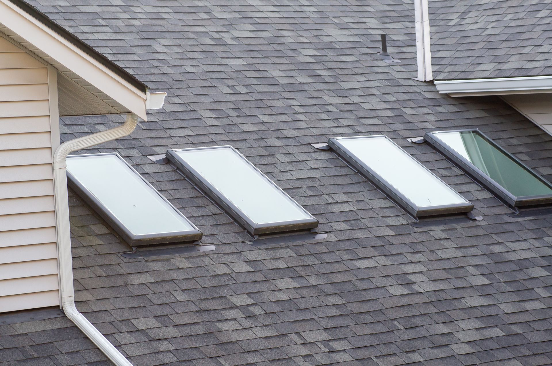Four rectangular skylights installed in a row on a grey shingled residential roof.