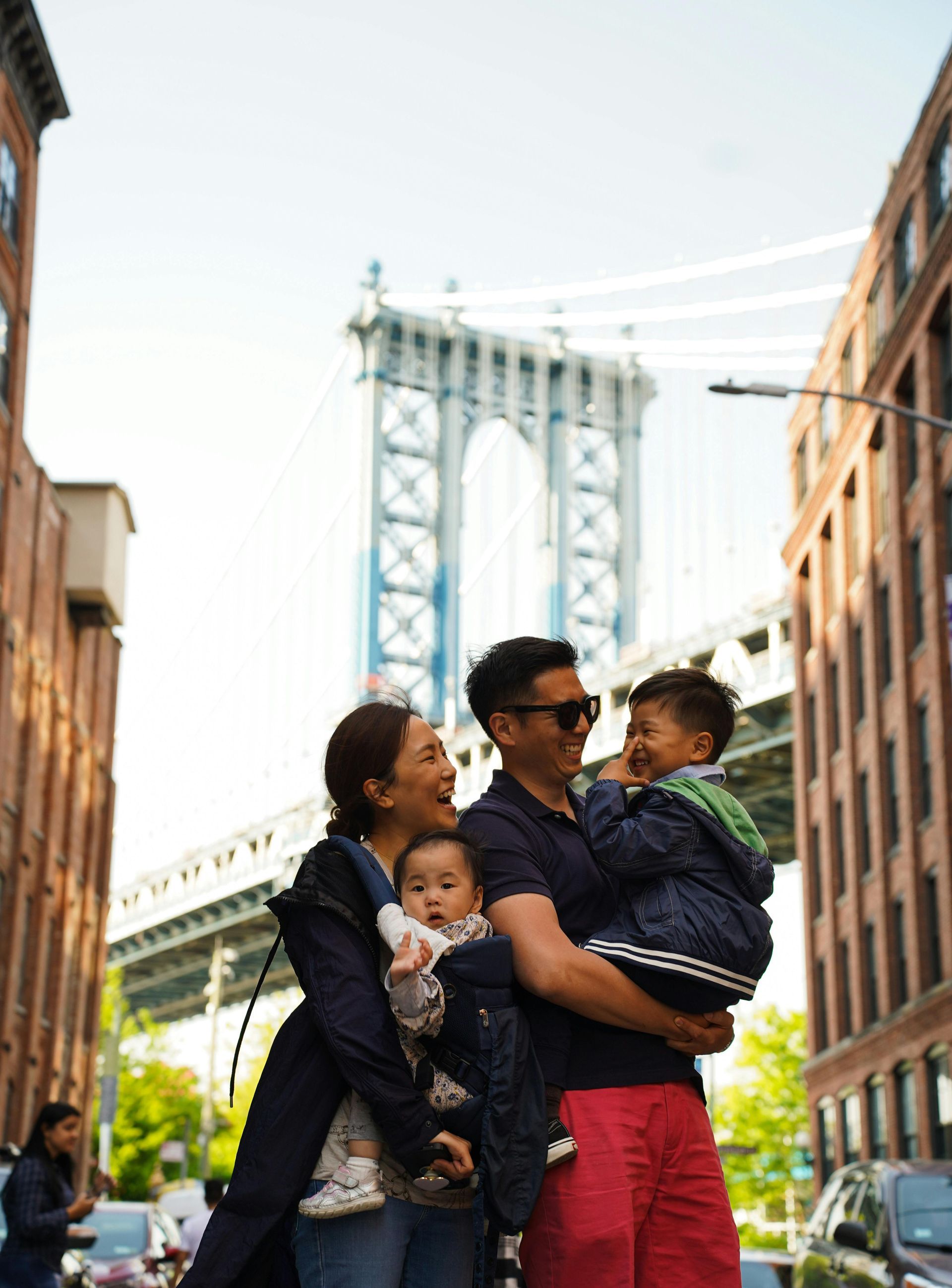 A man and woman are holding two children in front of a bridge.