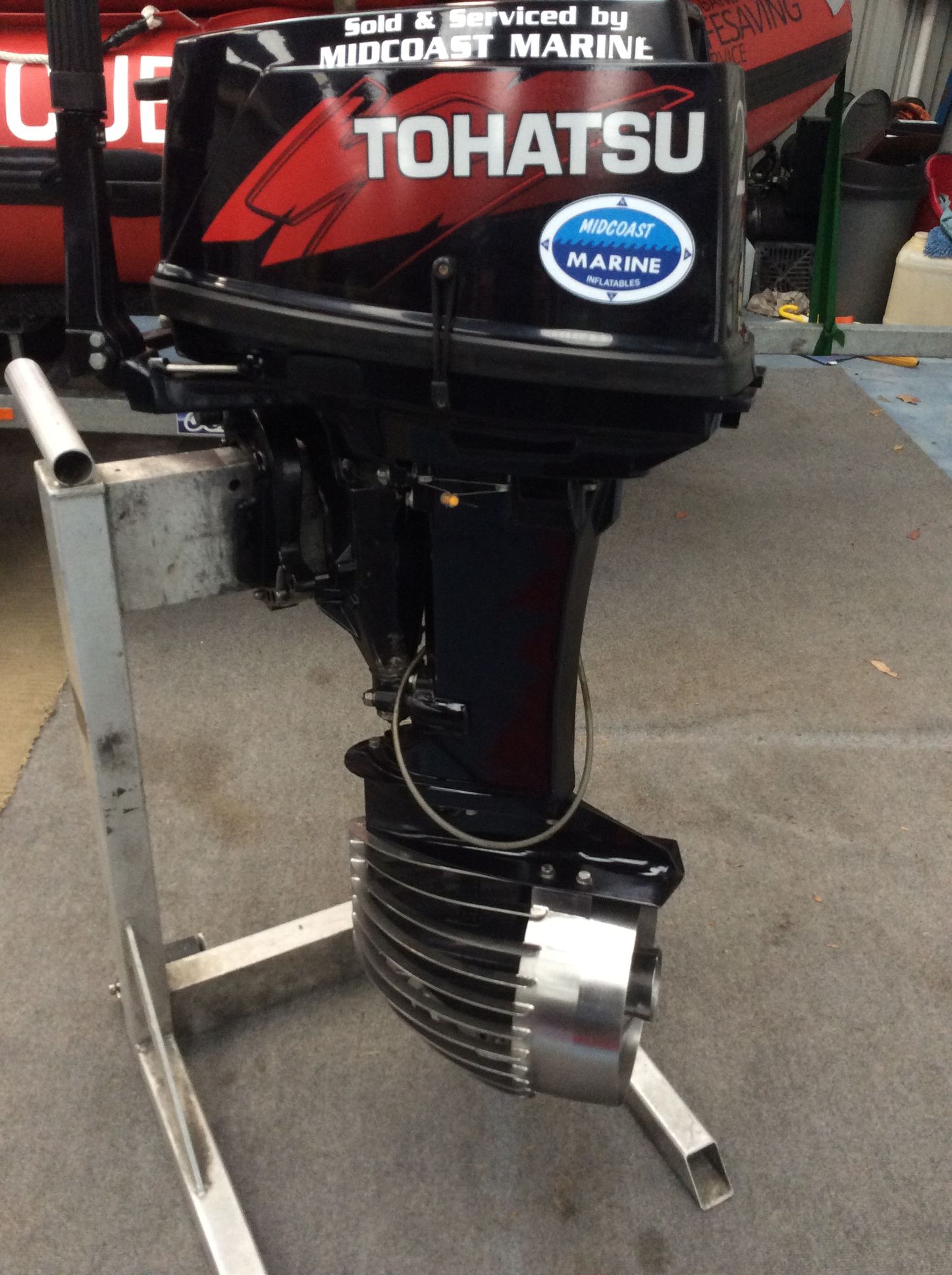 A black Tohatsu outboard motor mounted on a metal stand, displayed indoors on a concrete floor.