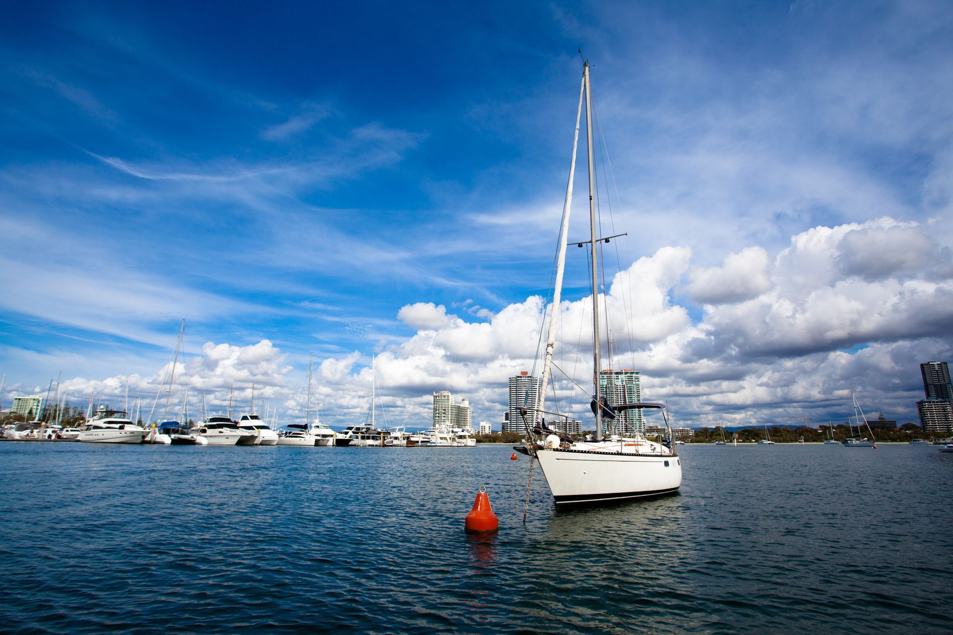 A sailboat gliding across calm water under a blue sky with white clouds.