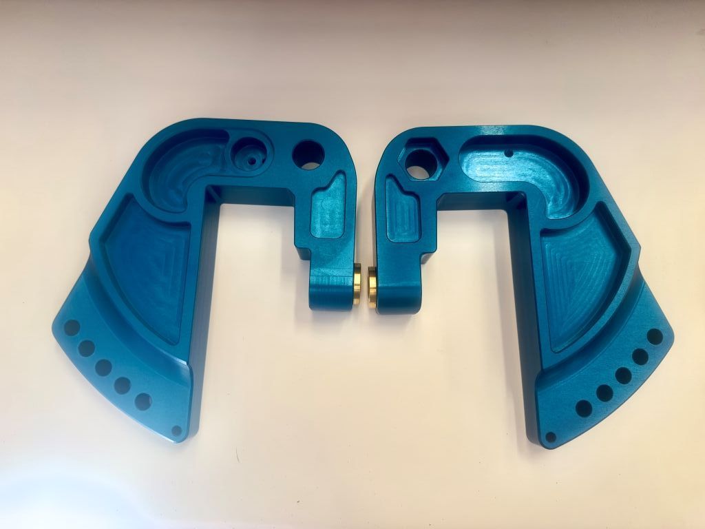 Two blue plastic mechanical parts mirrored side by side on a white surface.