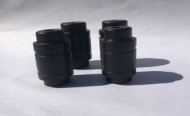 Four black camera lens-like cylinders on a white surface, casting long shadows.