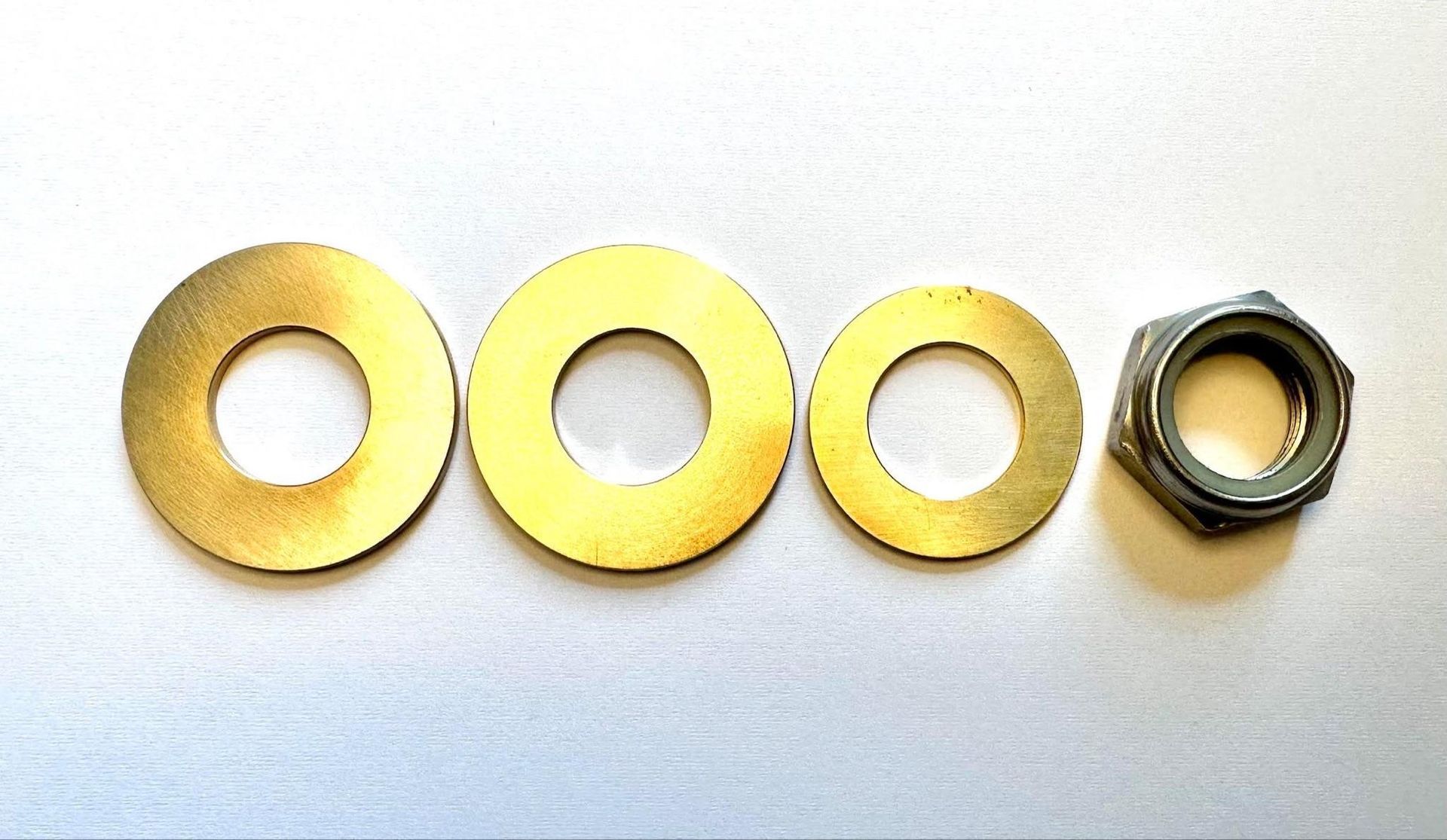 Four metal washers and a hex nut arranged in a row on a light surface