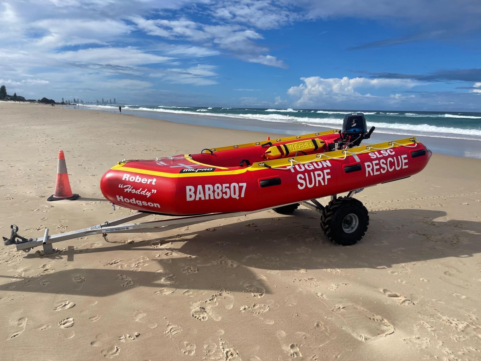 Red surf rescue rescue sled on a sandy beach beside the ocean, with clouds overhead
