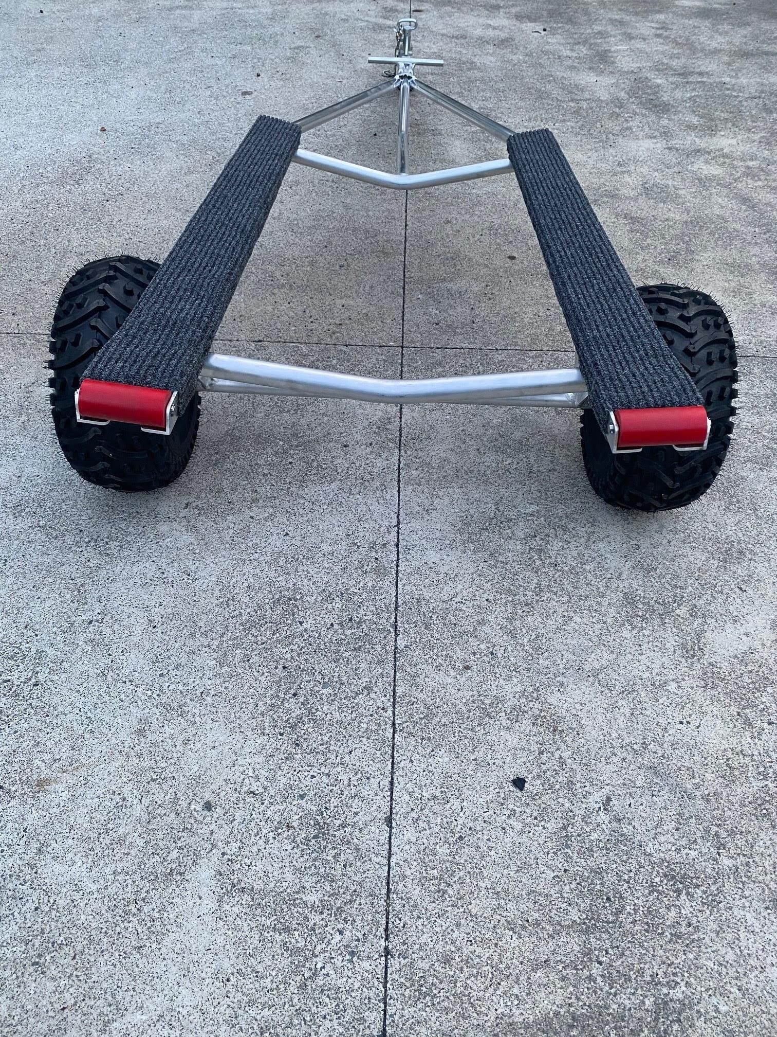 Silver trailer dolly with two black wheels and red reflectors on a concrete surface