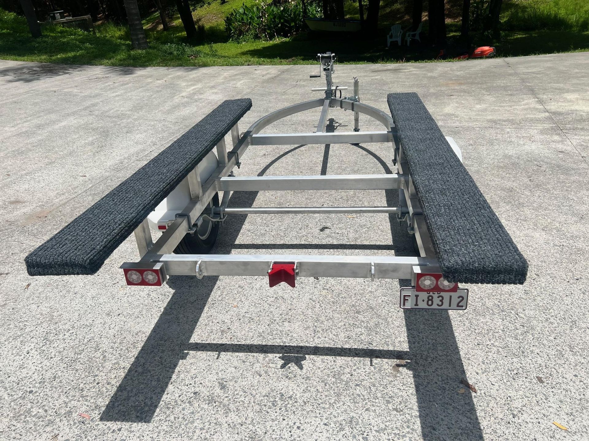 Empty boat trailer with black bunks on a gravel lot, viewed from the rear.