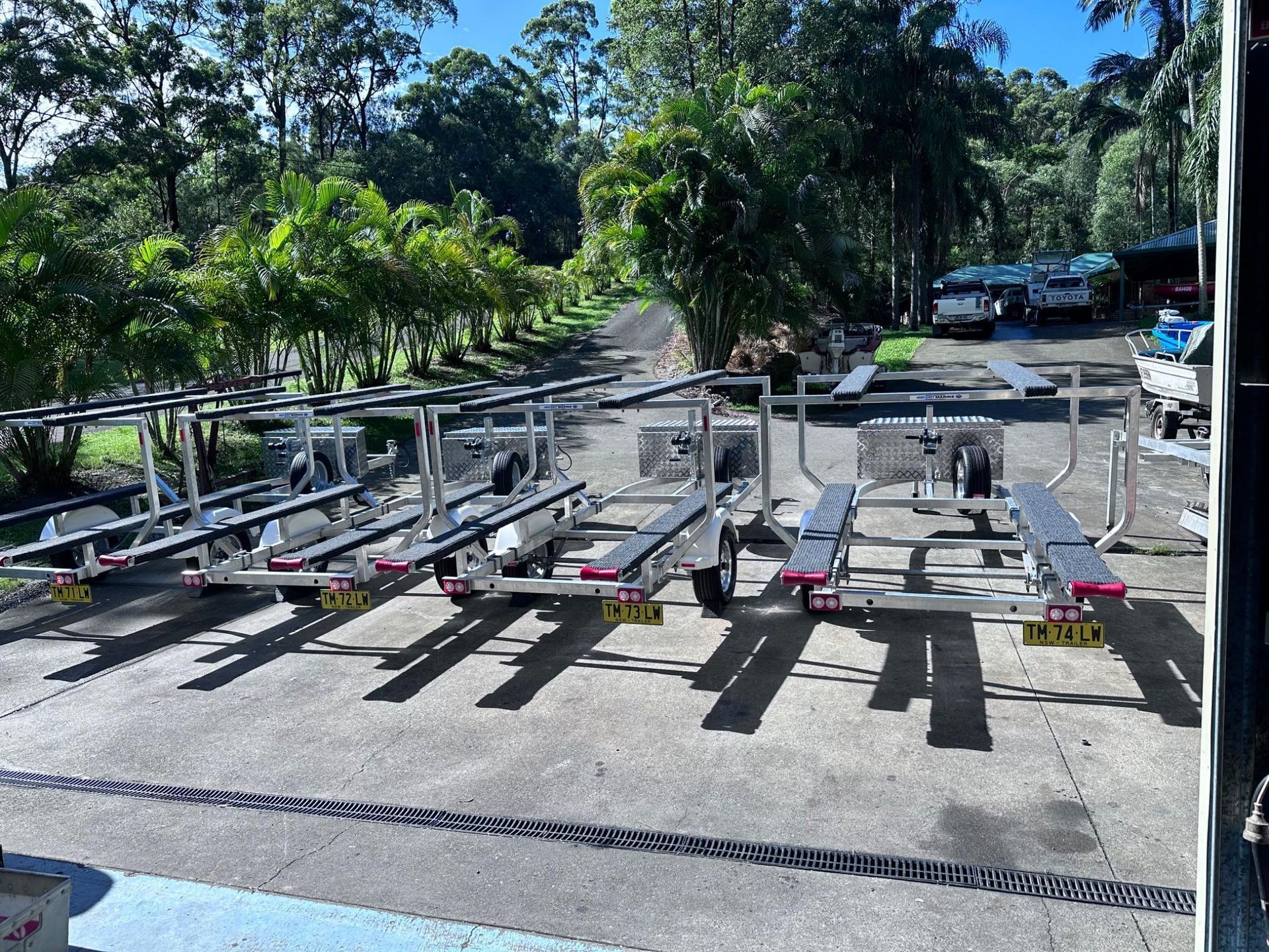 Row of metal dog carts on a paved outdoor lot beside trees and a road.