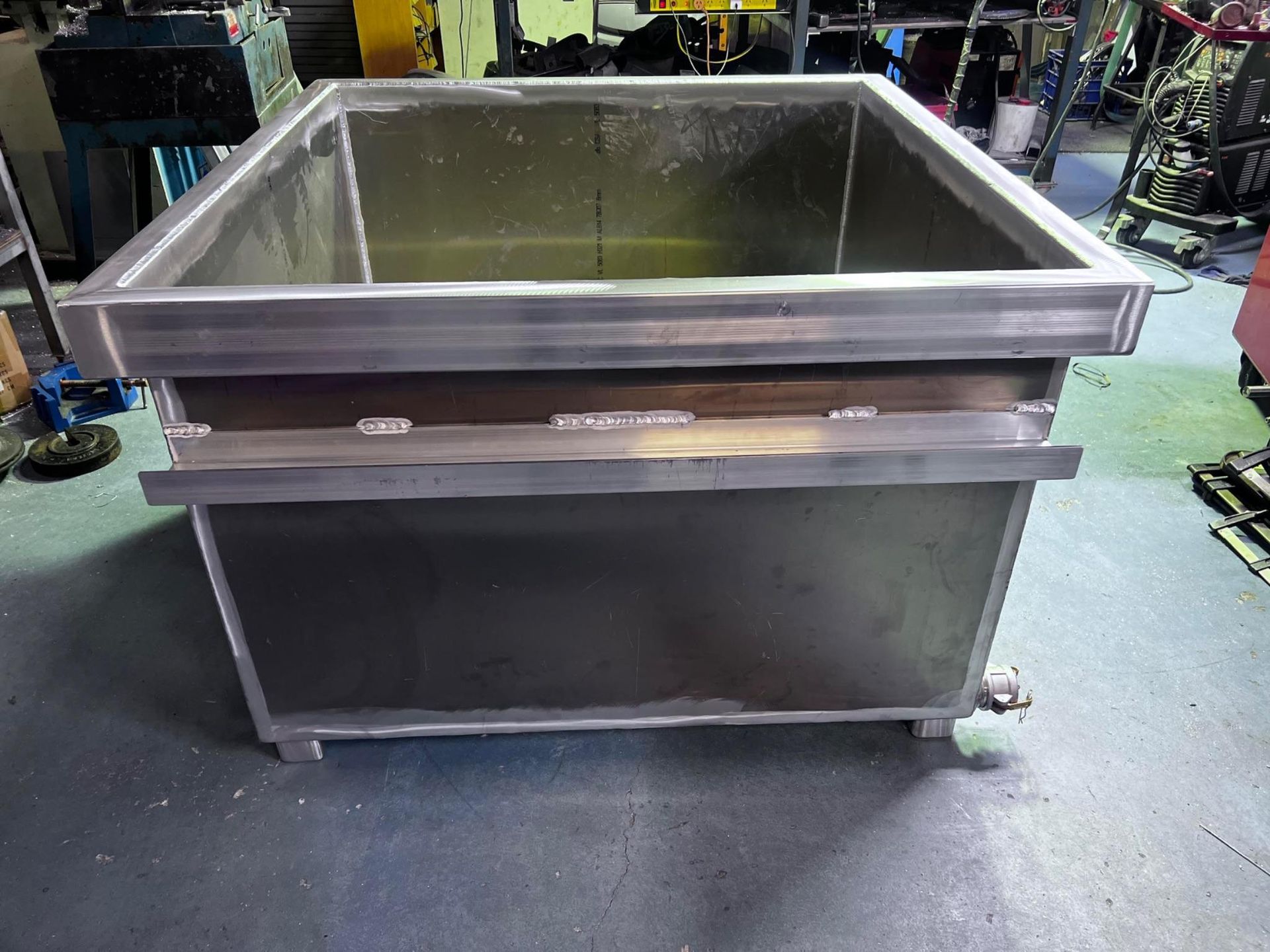 Large stainless steel industrial tank on a factory floor with wheels and a wide open top.