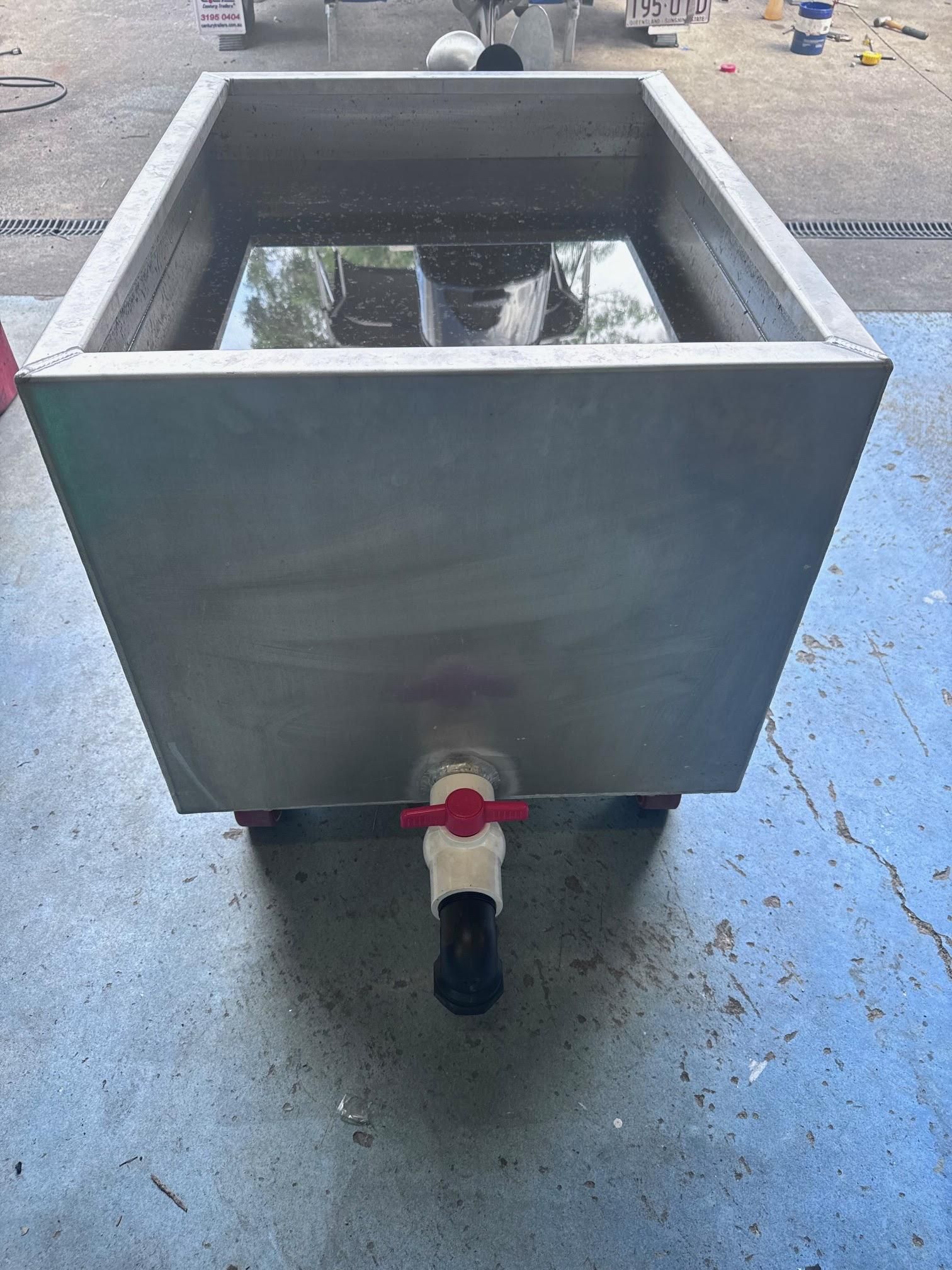 Metal square tank with water and a red valve on a black pipe in a workshop