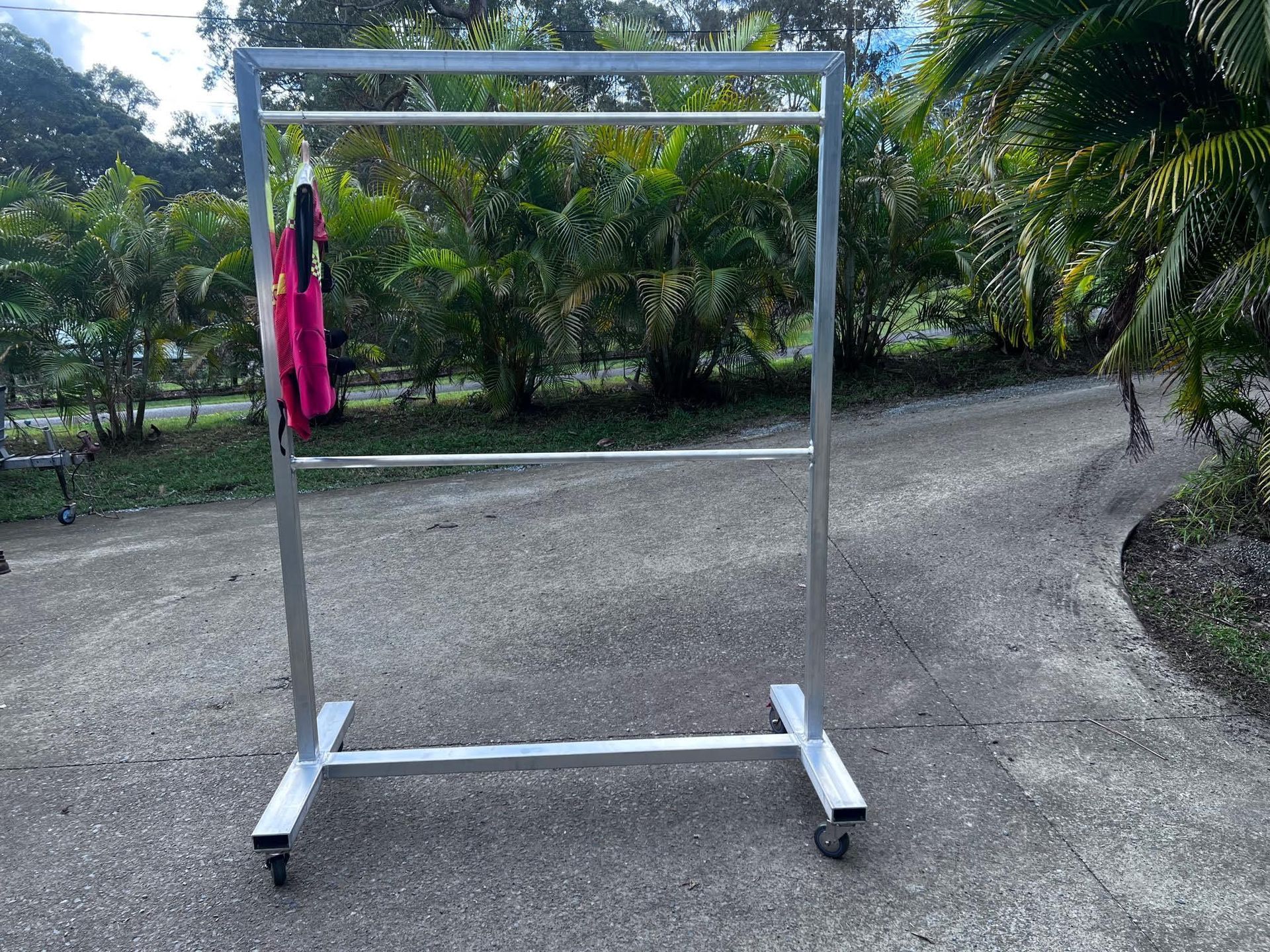 Metal clothing rack with a pink garment hanging outdoors on a gravel path.