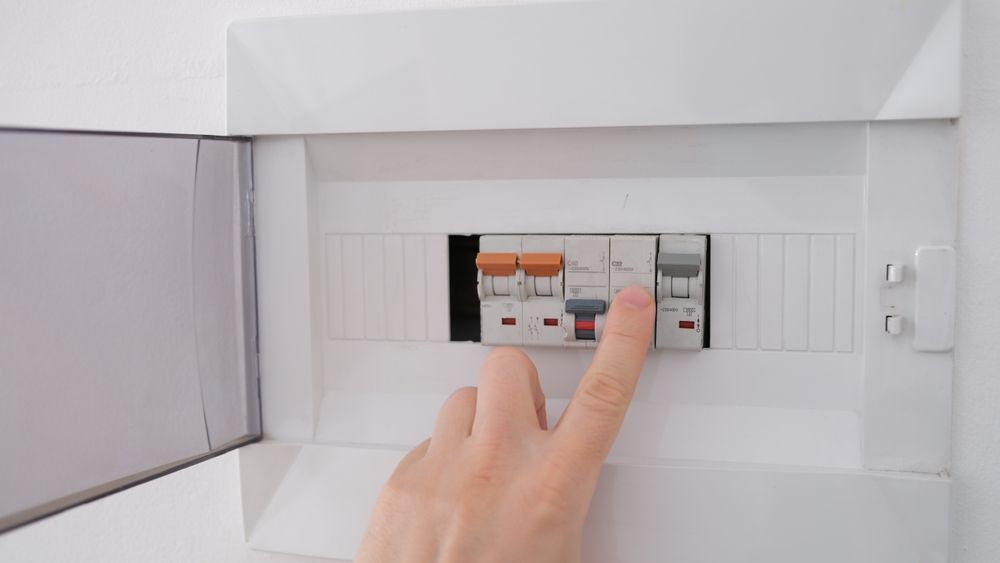 Person's Finger Flips a Circuit Breaker Switch in A White Electrical Panel Box — Townsville Electrical and Appliance Repairs In Aitkenvale, QLD