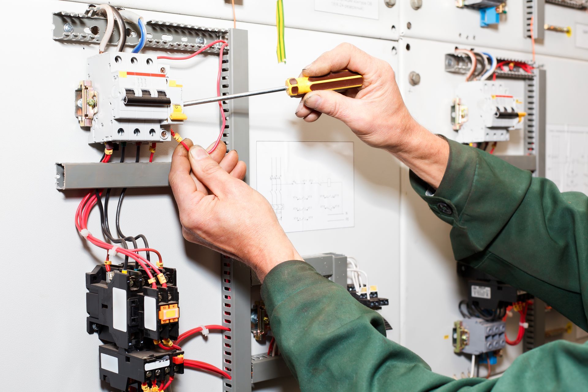 Electrician in Green Uniform Working on Electrical Panel with Screwdriver — Townsville Electrical and Appliance Repairs In Hermit Park, QLD