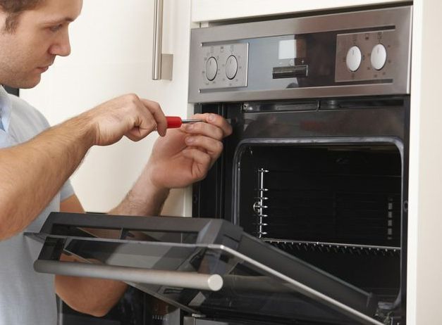 Man Repairs Oven with A Screwdriver in A Kitchen — Townsville Electrical and Appliance Repairs In Aitkenvale, QLD