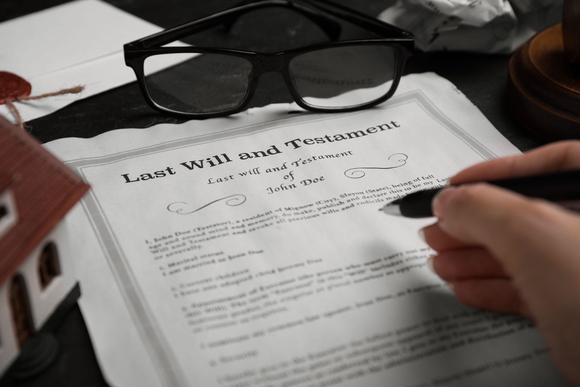 Hand filling out a legal document beside black glasses and a red model house