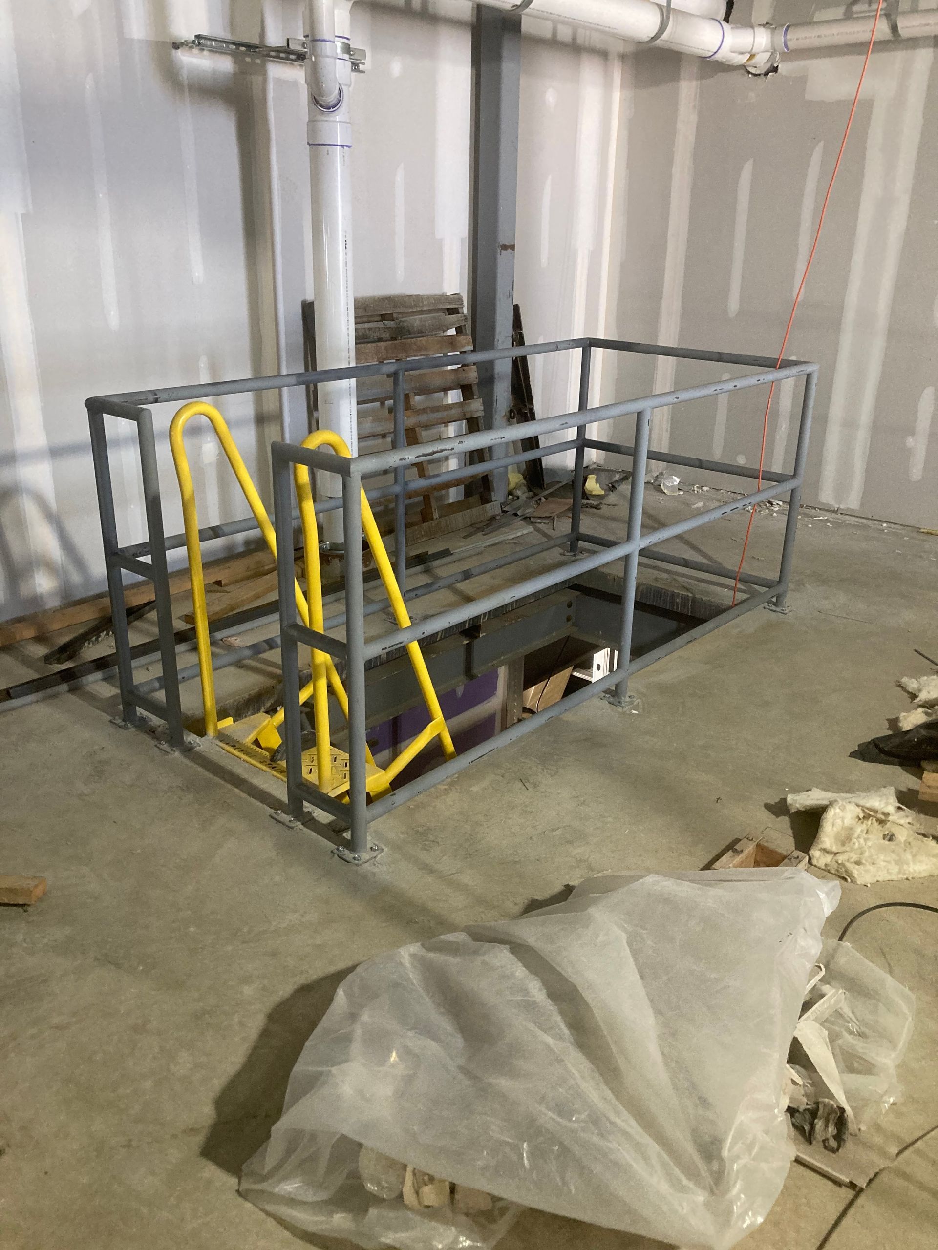 Yellow and grey safety cage surrounding an opening in a concrete floor, in a construction setting.