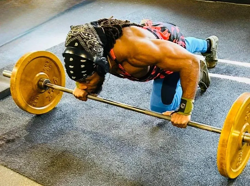 Athlete doing a barbell deadlift on a gym floor, leaning low over yellow weights.