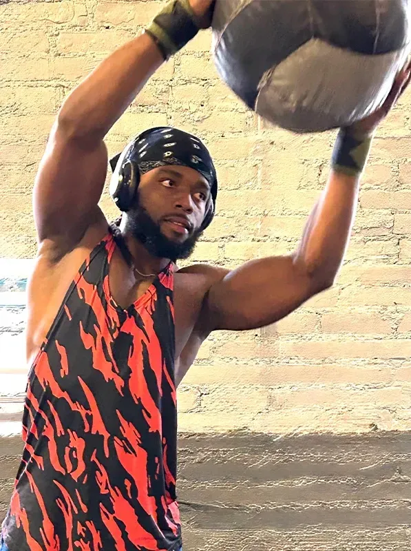 Man lifting a medicine ball overhead outdoors against a brick wall