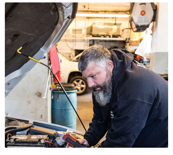 Mechanic working under a raised hood in an auto repair shop, focused on engine repairs | Expert Auto Service & Licensing
