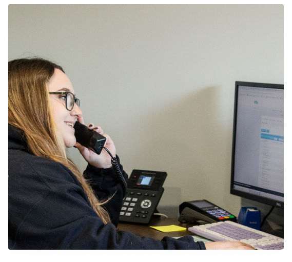 Woman on the phone at a desk, looking at a computer monitor. | Expert Auto Service & Licensing