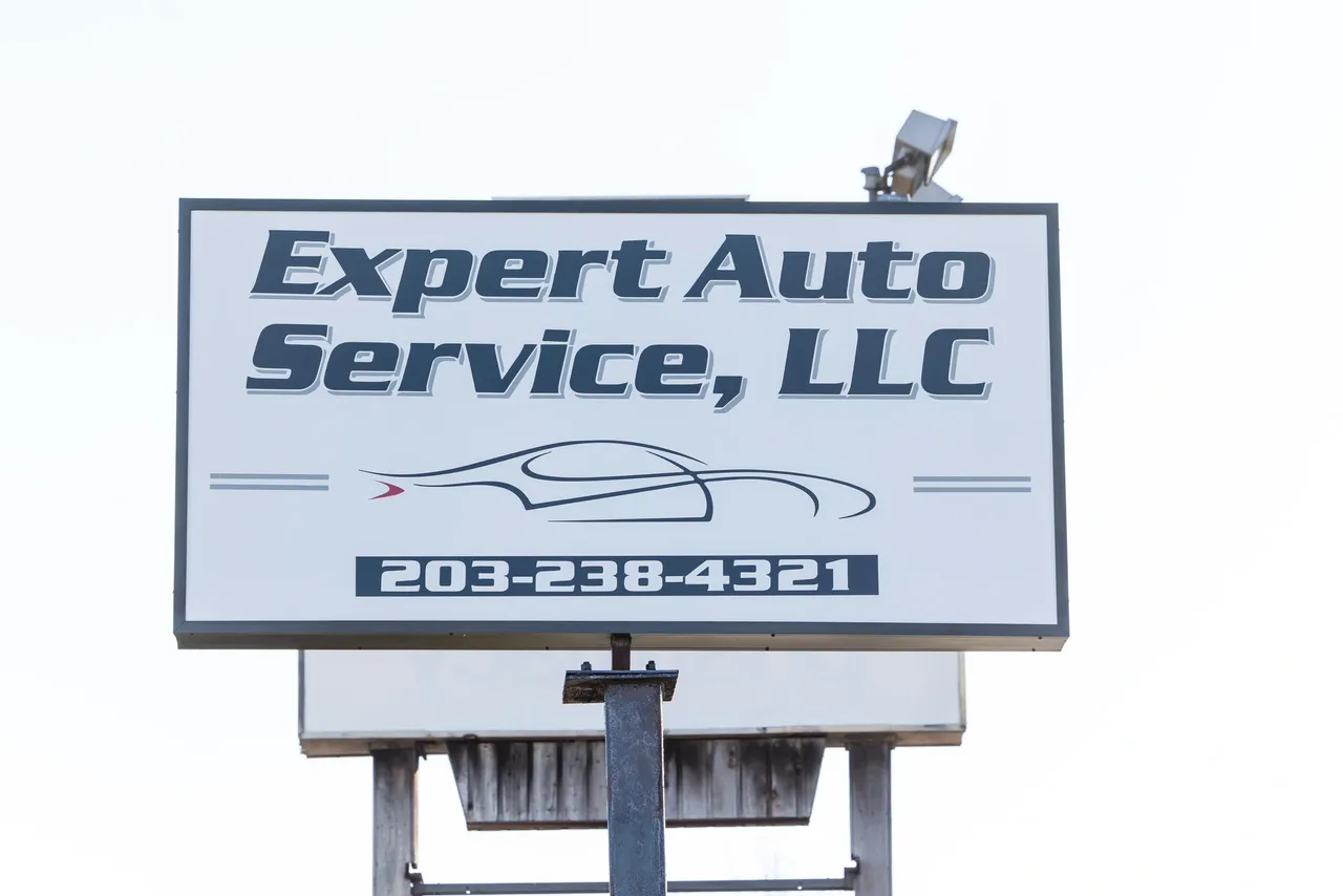 Expert Auto Service, LLC sign with phone number 203-318-4321 on a pole outdoors | Expert Auto Service & Licensing