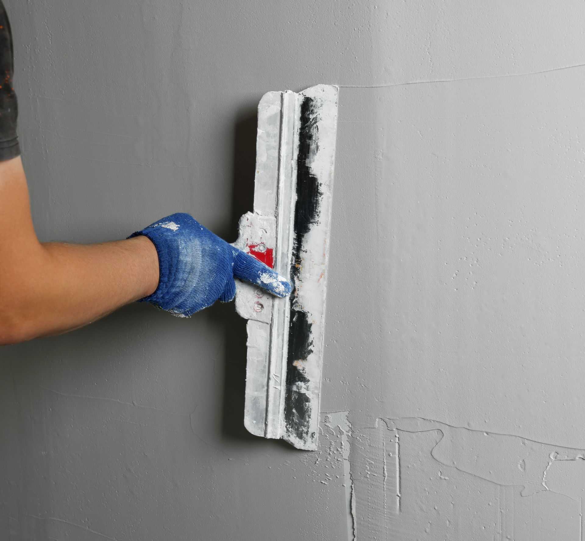 Gloved hand smoothing gray plaster on a wall with a trowel