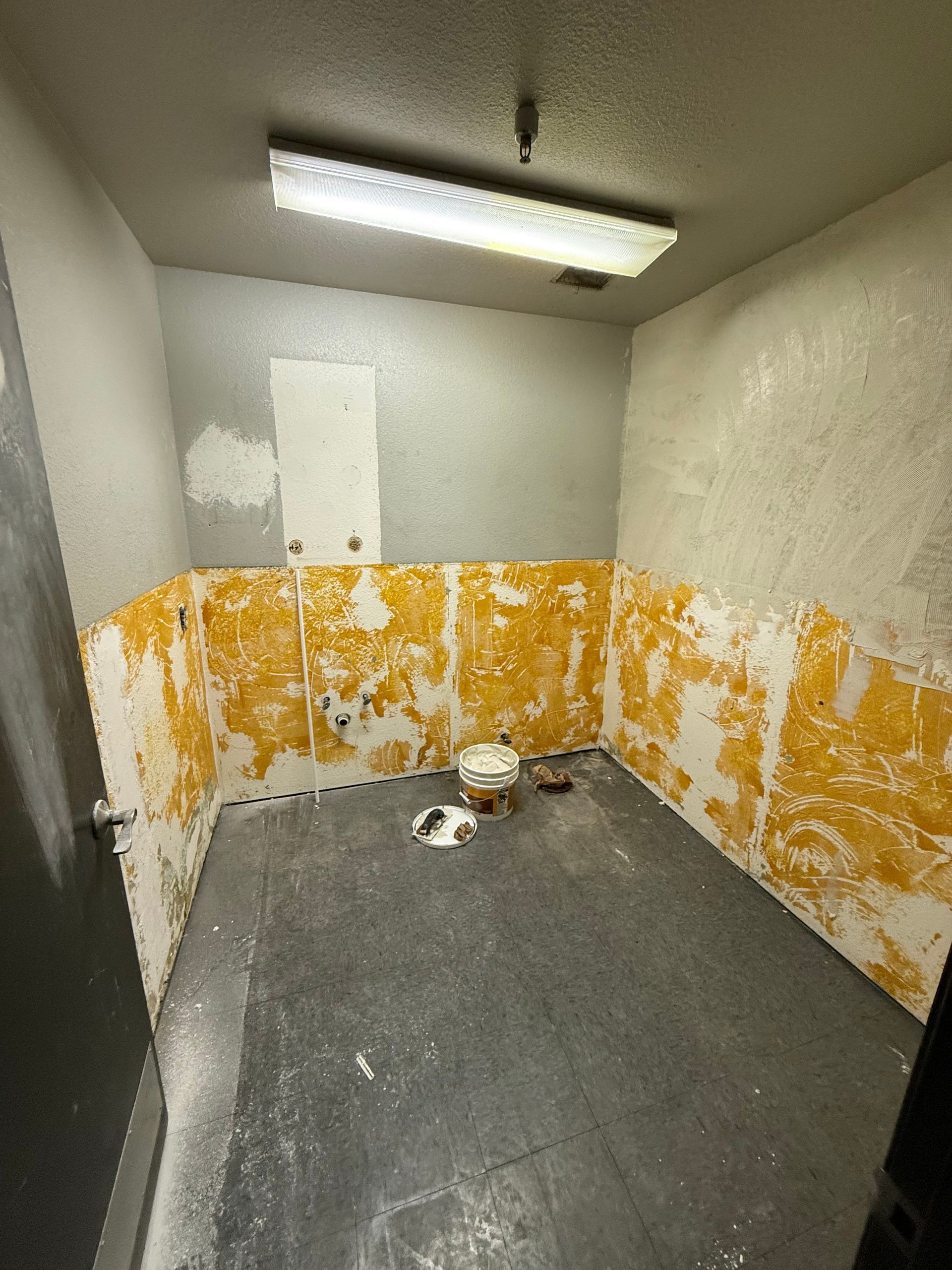 Small empty room with peeling yellow paint, gray floor, and fluorescent ceiling light.